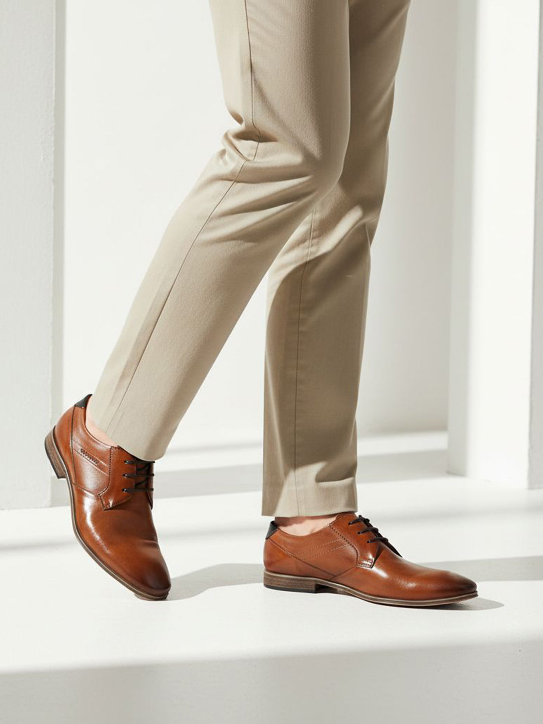 bugatti Morino I cognac brown leather formal shoes with black laces, styled with tan slacks.
