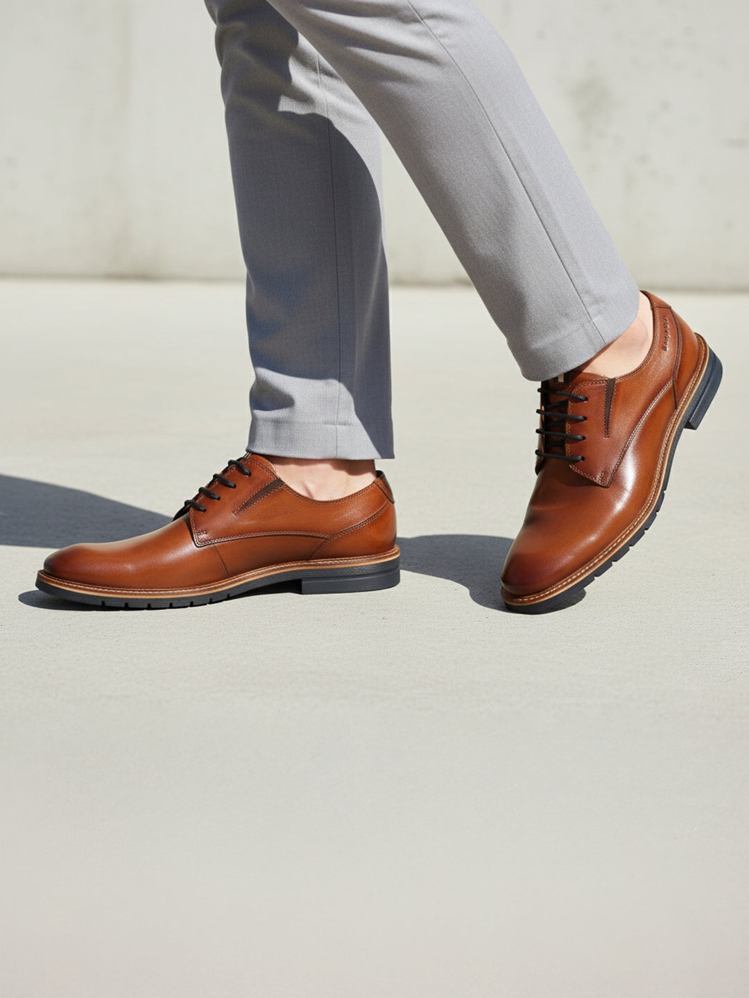 bugatti Merlo cognac leather dress shoes with black laces, paired with gray dress pants.
