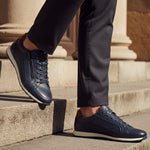 Lifestyle view of bugatti Thorello dark blue premium leather sneakers with side zip, paired with dark dress pants.
