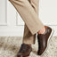 Lifestyle shot of bugatti Thorello brown premium leather sneakers with white soles, styled with tan trousers on a carpet.
