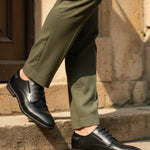 bugatti Menello black leather formal shoes with a textured finish, shown on a person with green dress pants.
