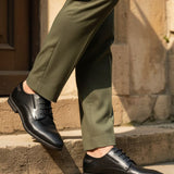 bugatti Menello black leather formal shoes with a textured finish, shown on a person with green dress pants.
