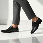 Side view of black bugatti leather derby shoes, paired with gray dress pants on a white marble floor.