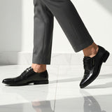 Side view of black bugatti leather derby shoes, paired with gray dress pants on a white marble floor.