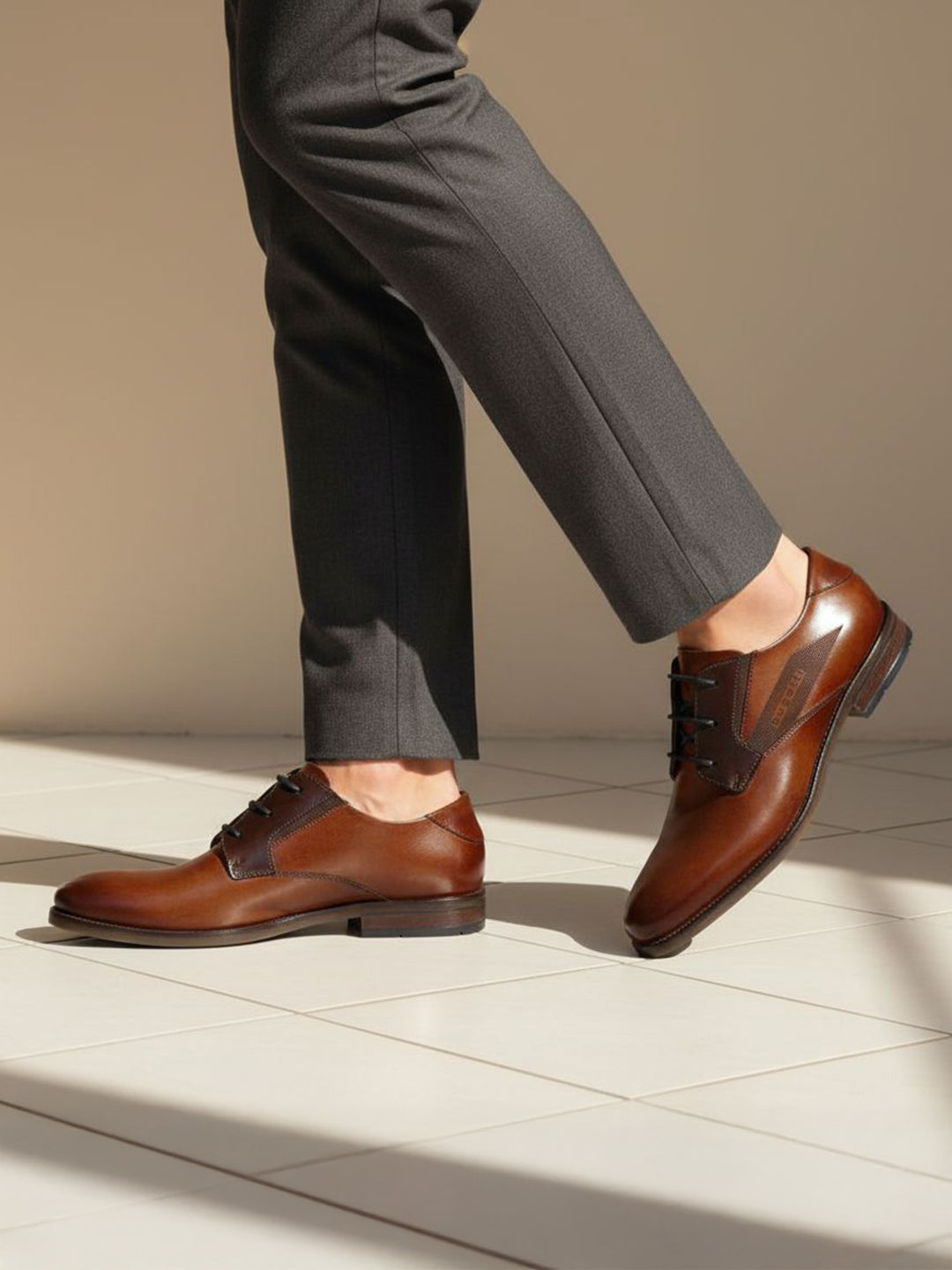 bugatti Sula cognac leather derby shoes, paired with gray dress pants, on a tiled surface.
