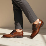 bugatti Sula cognac leather derby shoes, paired with gray dress pants, on a tiled surface.
