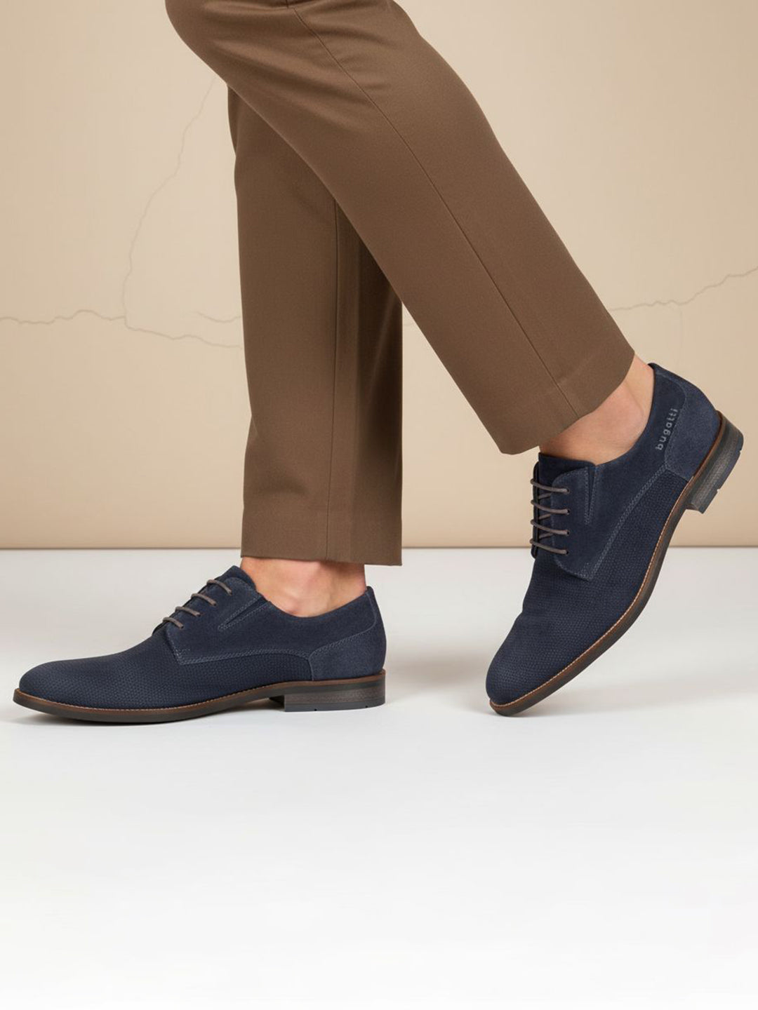 Lifestyle image of bugatti Sula dark blue leather derby shoes with brown laces, worn with brown trousers.