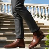 bugatti Amros Cognac Premium Leather Comfort Chelsea Boots with side zipper, worn with grey slacks on stairs.
