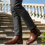 bugatti Amros Cognac Premium Leather Comfort Chelsea Boots with side zipper, worn with grey slacks on stairs.
