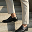 Black leather penny loafers by bugatti with a low heel, worn with light colored pants while standing on gray stairs.