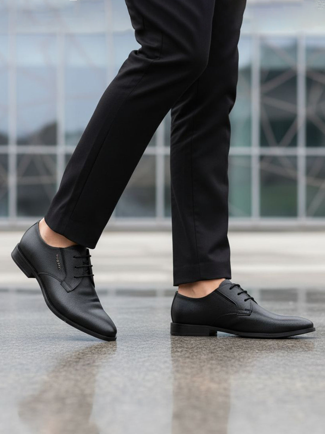 Cropped lifestyle shot of bugatti black leather formal derby shoes with textured design, paired with black dress pants.

