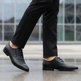 Cropped lifestyle shot of bugatti black leather formal derby shoes with textured design, paired with black dress pants.
