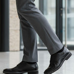 Lifestyle close-up of black bugatti Mero formal leather derby shoes, gray dress pants, and black socks.
