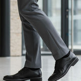 Lifestyle close-up of black bugatti Mero formal leather derby shoes, gray dress pants, and black socks.
