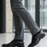 Lifestyle close-up of black bugatti Mero formal leather derby shoes, gray dress pants, and black socks.

