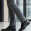 Lifestyle close-up of black bugatti Mero formal leather derby shoes, gray dress pants, and black socks.
