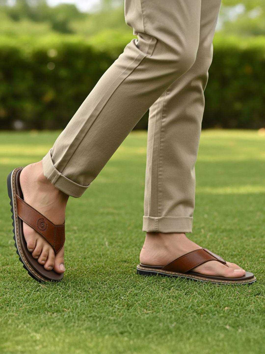 bugatti Limon cognac leather thong sandals, with a black ridged sole, worn with khaki trousers on grass.
