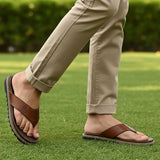 bugatti Limon cognac leather thong sandals, with a black ridged sole, worn with khaki trousers on grass.
