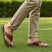 bugatti Limon cognac leather thong sandals, with a black ridged sole, worn with khaki trousers on grass.
