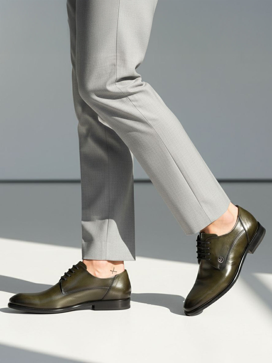 bugatti Mansueto Flex Derby shoes in dark green premium leather, worn with grey dress pants and a small ankle tattoo.