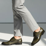 bugatti Mansueto Flex Derby shoes in dark green premium leather, worn with grey dress pants and a small ankle tattoo.