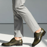 bugatti Mansueto Flex Derby shoes in dark green premium leather, worn with grey dress pants and a small ankle tattoo.