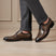 bugatti Livorno Flex Evo dark grey leather formal shoes, with brogue detailing, styled with grey trousers.
