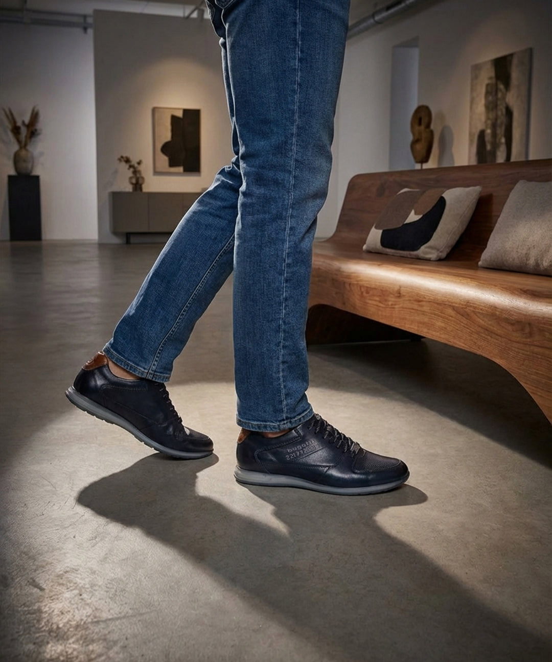 Lifestyle view of bugatti Thorello dark blue leather sneakers with blue jeans and casual indoor setting.
