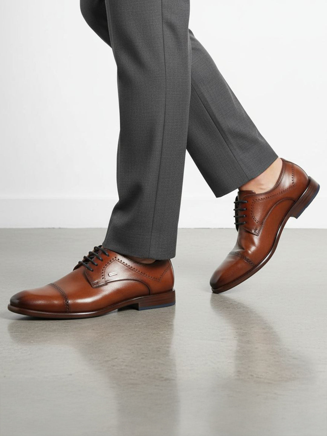 Lifestyle shot of bugatti Mansueto Flex Cognac leather derby formal shoes with black laces and blue sole accent.
