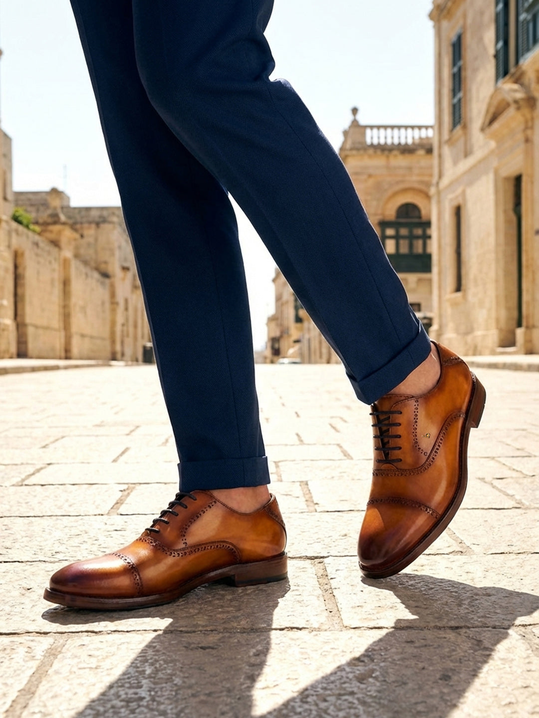 bugatti Liverta yellow leather oxford shoes with dark laces and decorative stitching worn with dark blue pants.
