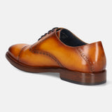 Yellow leather Oxford shoe by bugatti, featuring brogue detailing, and a stacked heel, shown in a back-side view.
