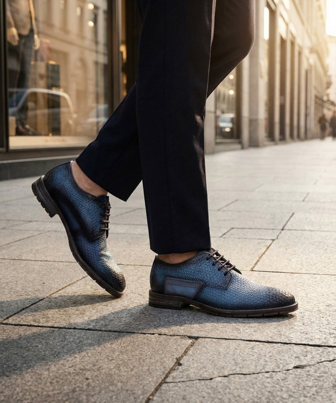 Lifestyle shot of bugatti blue premium leather comfort derby dress shoes worn with dark pants on a city street.
