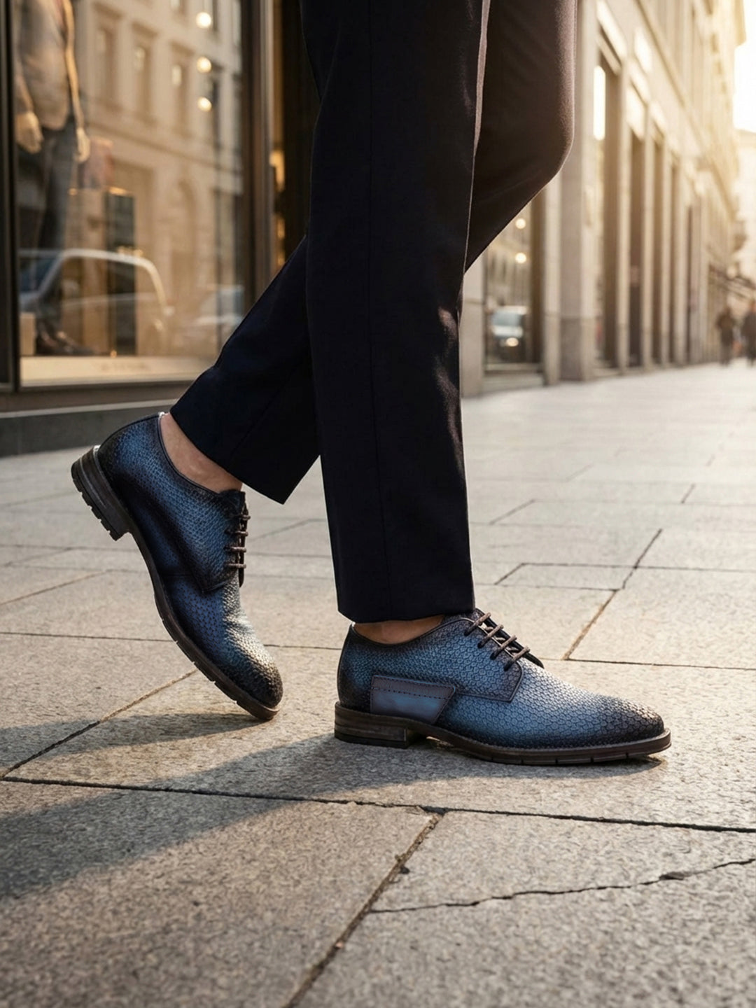 Lifestyle shot of bugatti blue premium leather comfort derby dress shoes worn with dark pants on a city street.
