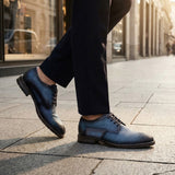 Lifestyle shot of bugatti blue premium leather comfort derby dress shoes worn with dark pants on a city street.
