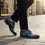 Lifestyle shot of bugatti blue premium leather comfort derby dress shoes worn with dark pants on a city street.
