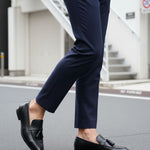 Cropped view of bugatti Rico black leather slip-on dress shoes with tassels, worn with navy trousers.
