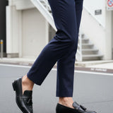 Cropped view of bugatti Rico black leather slip-on dress shoes with tassels, worn with navy trousers.
