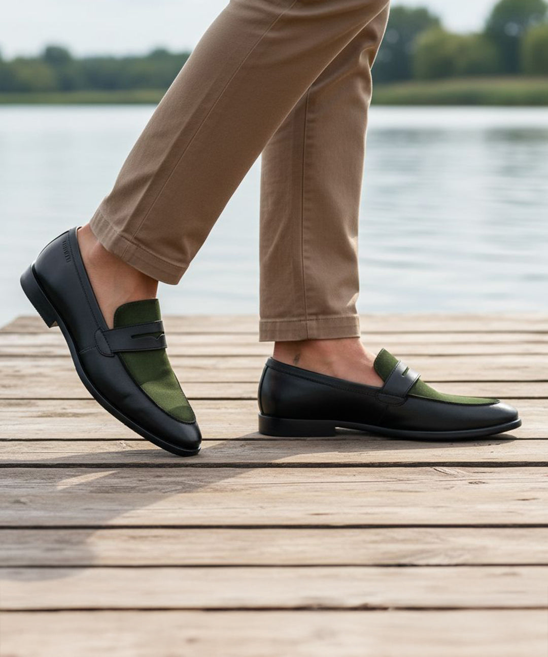 Lifestyle view of bugatti Rico black leather loafers with green trim, worn with tan pants on a wooden boardwalk.
