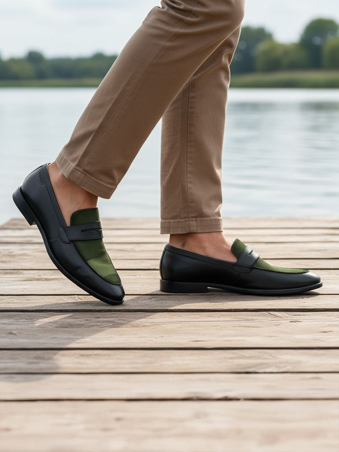 Lifestyle view of bugatti Rico black leather loafers with green trim, worn with tan pants on a wooden boardwalk.
