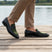 Lifestyle view of bugatti Rico black leather loafers with green trim, worn with tan pants on a wooden boardwalk.
