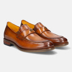 Tan leather penny loafers by bugatti, featuring a golden metal logo on the upper strap and a sleek silhouette.
