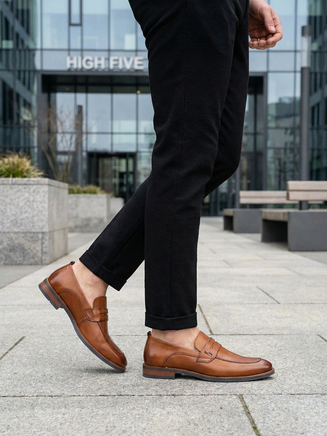 bugatti Sula Revo cognac penny loafers in premium leather, paired with black textured pants, outdoor setting.
