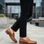 bugatti Sula Revo cognac penny loafers in premium leather, paired with black textured pants, outdoor setting.
