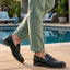bugatti Laziano black leather loafers with a buckle, worn with green pants near a pool.
