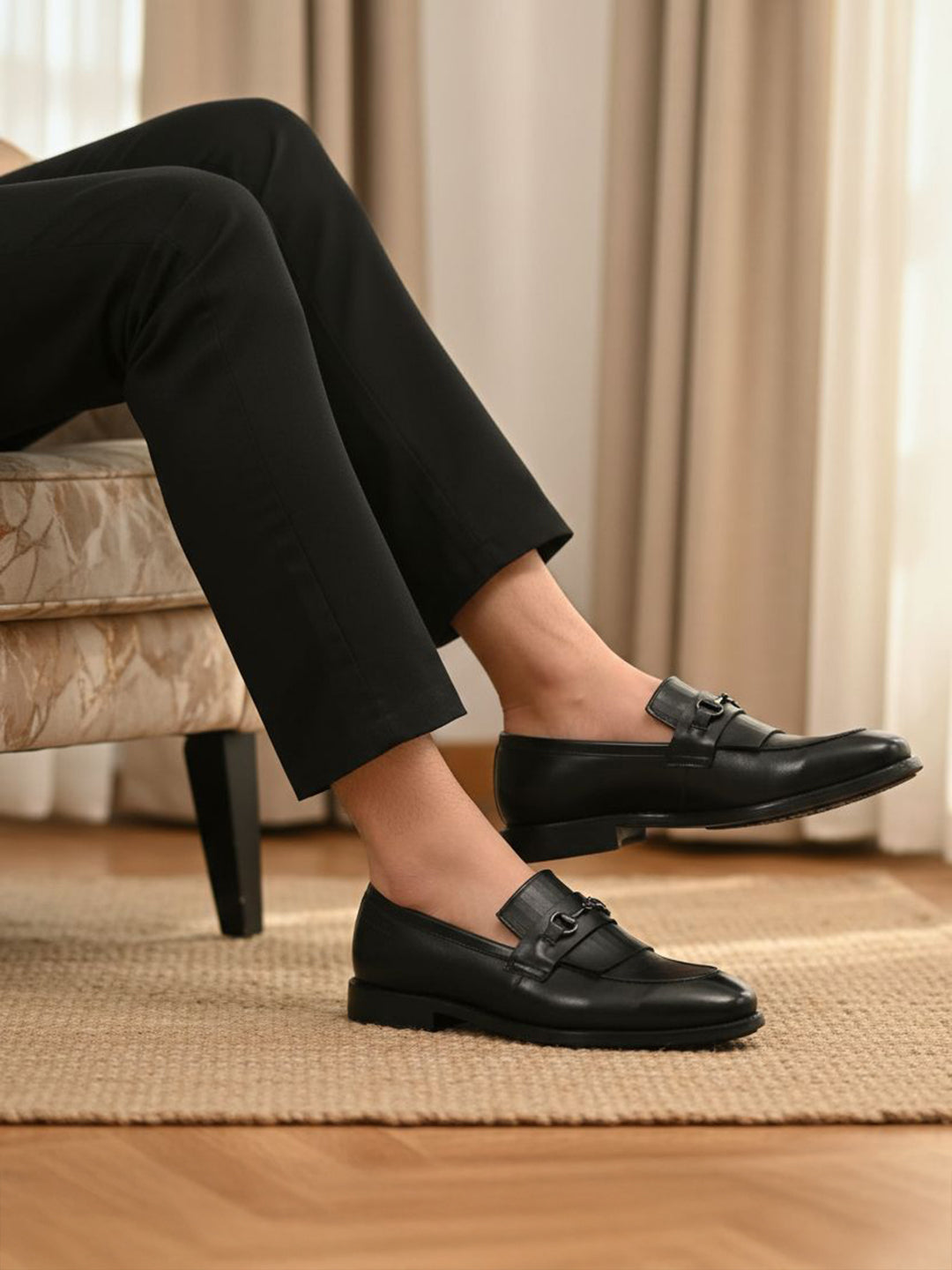 Lifestyle shot of black bugatti leather slip-on dress shoes, worn with black pants, and displayed on a rug.
