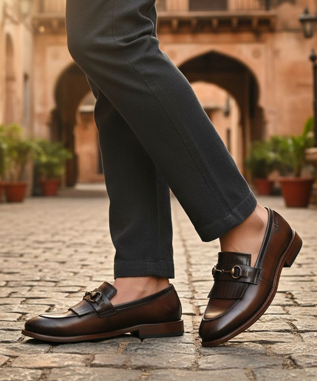 bugatti Liverta dark brown leather slip-on dress shoes with a decorative fringe, worn with gray pants.