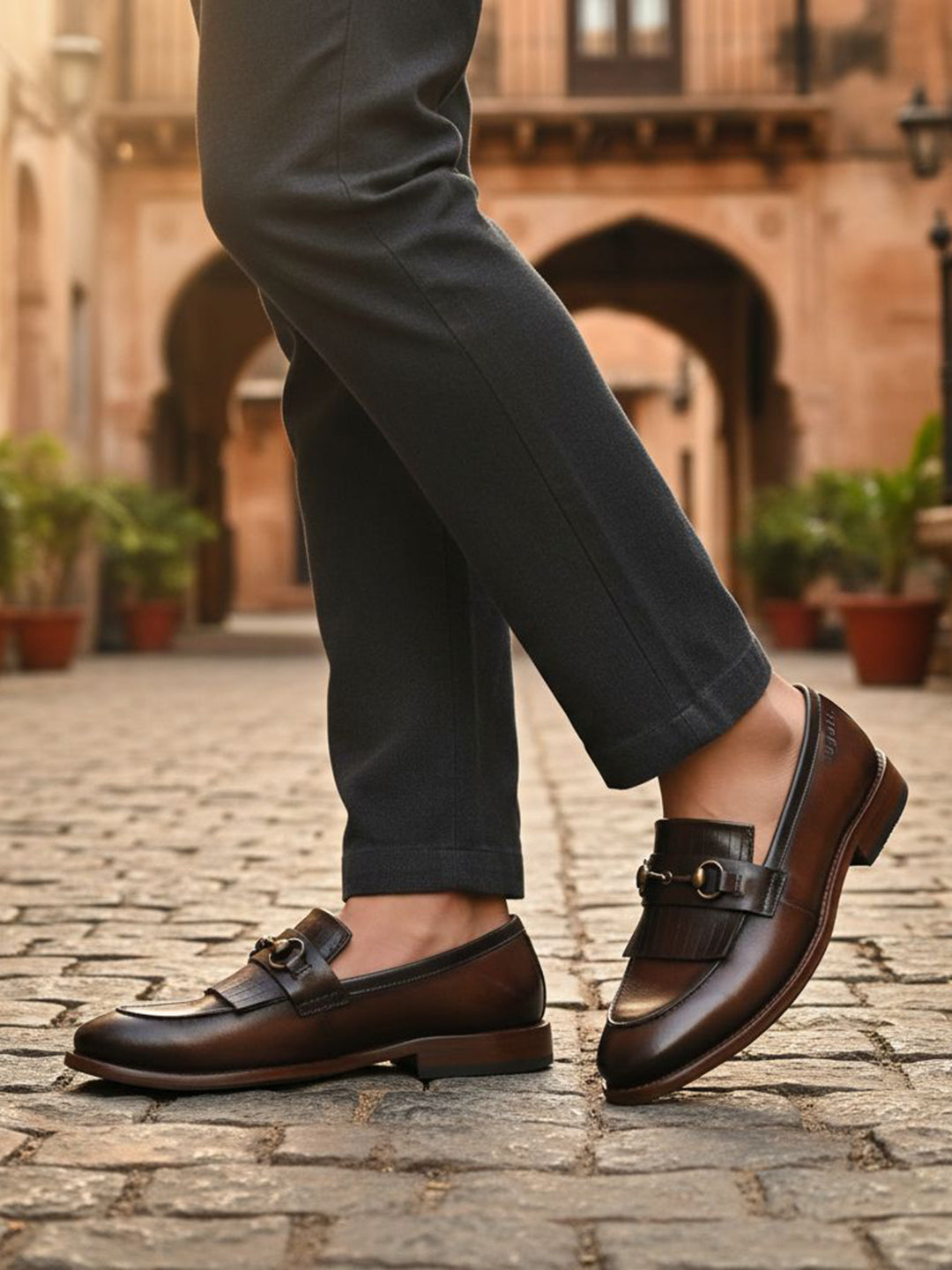 bugatti Liverta dark brown leather slip-on dress shoes with a decorative fringe, worn with gray pants.