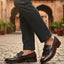bugatti Liverta dark brown leather slip-on dress shoes with a decorative fringe, worn with gray pants.