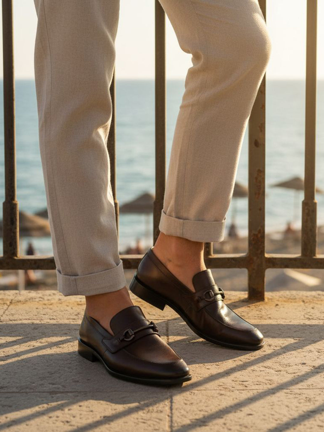 Bugatti Mansueto Bordo premium leather comfort slip-ons with a dark brown finish, styled with beige trousers.
