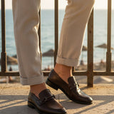 Bugatti Mansueto Bordo premium leather comfort slip-ons with a dark brown finish, styled with beige trousers.
